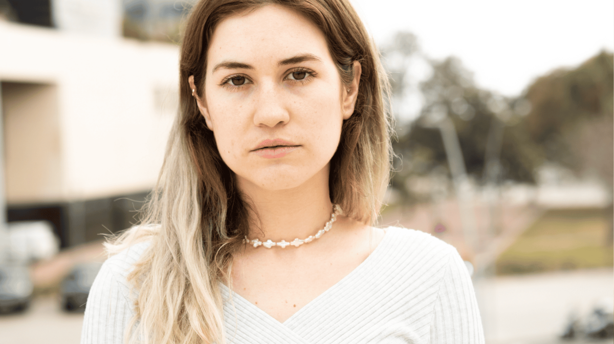 Junge Frau mit braunen Haaren und Perlenkette schaut ernst