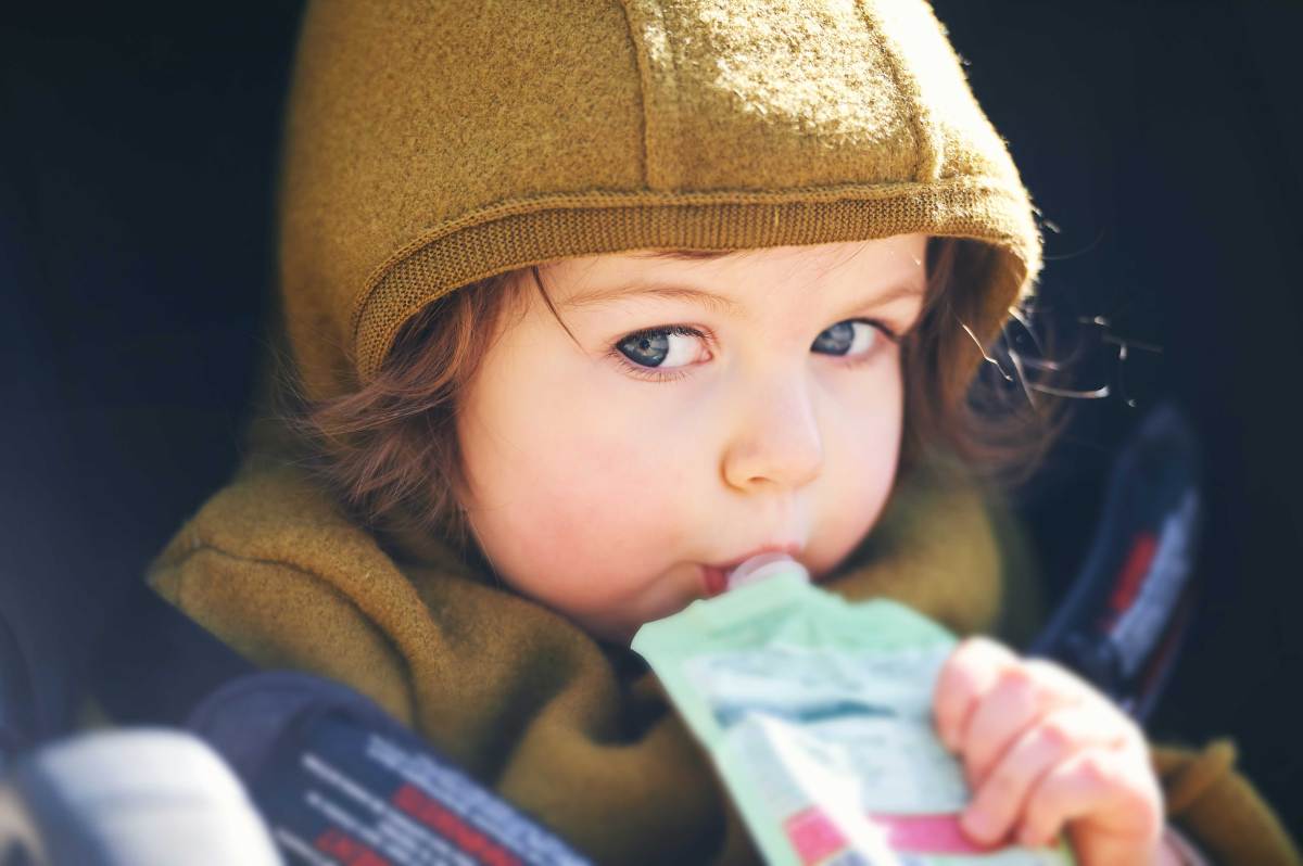 Nahaufnahme eines Kleinkind im Kinderwagen mit einem Quetschi im Mund.