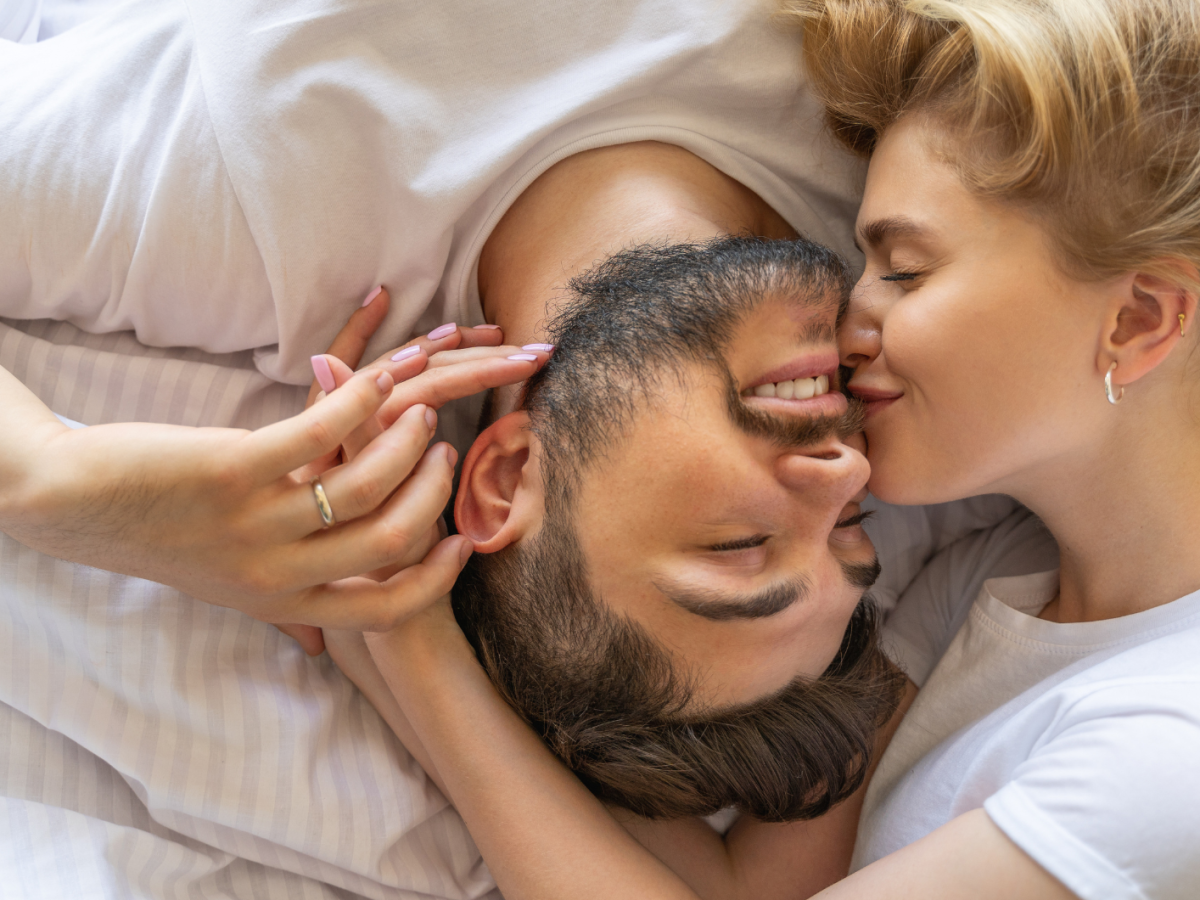Frau neben Mann im Bett, die ihn auf die Wange k&uuml;sst.