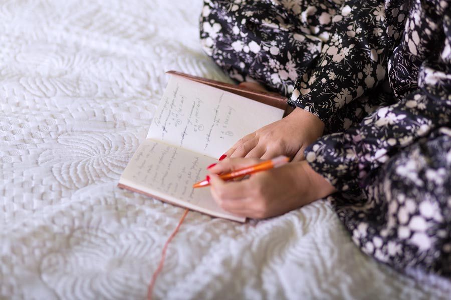 weibliche Person sitzt auf dem Bett und notiert etwas in einem Notizbuch