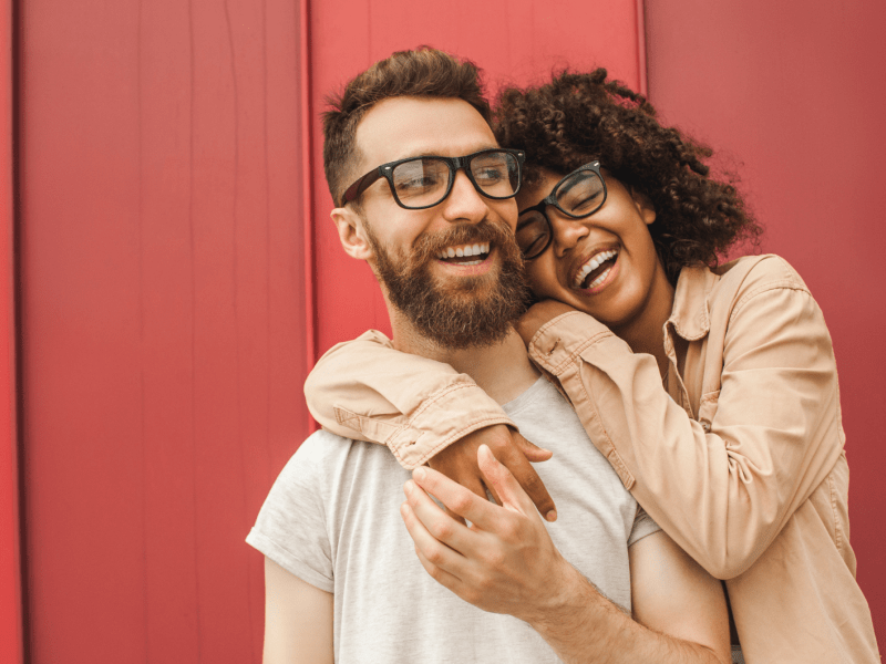 Pärchen, vor einer roten Wand, das sich lachend im Arm liegt.