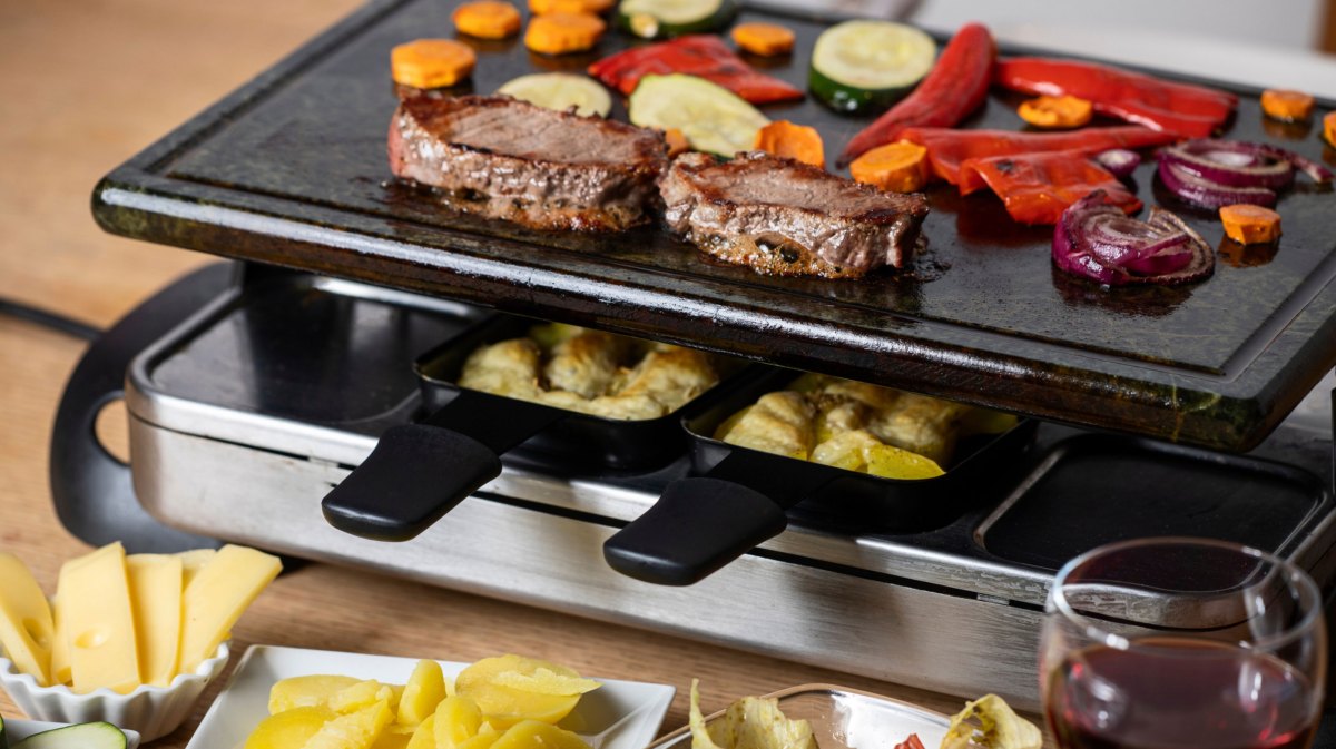 Raclette Mit 2 belegten Pfännchen und Fleisch und Gemüse auf dem heißen Stein