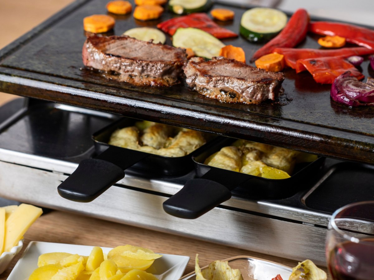 Raclette Mit 2 belegten Pfännchen und Fleisch und Gemüse auf dem heißen Stein