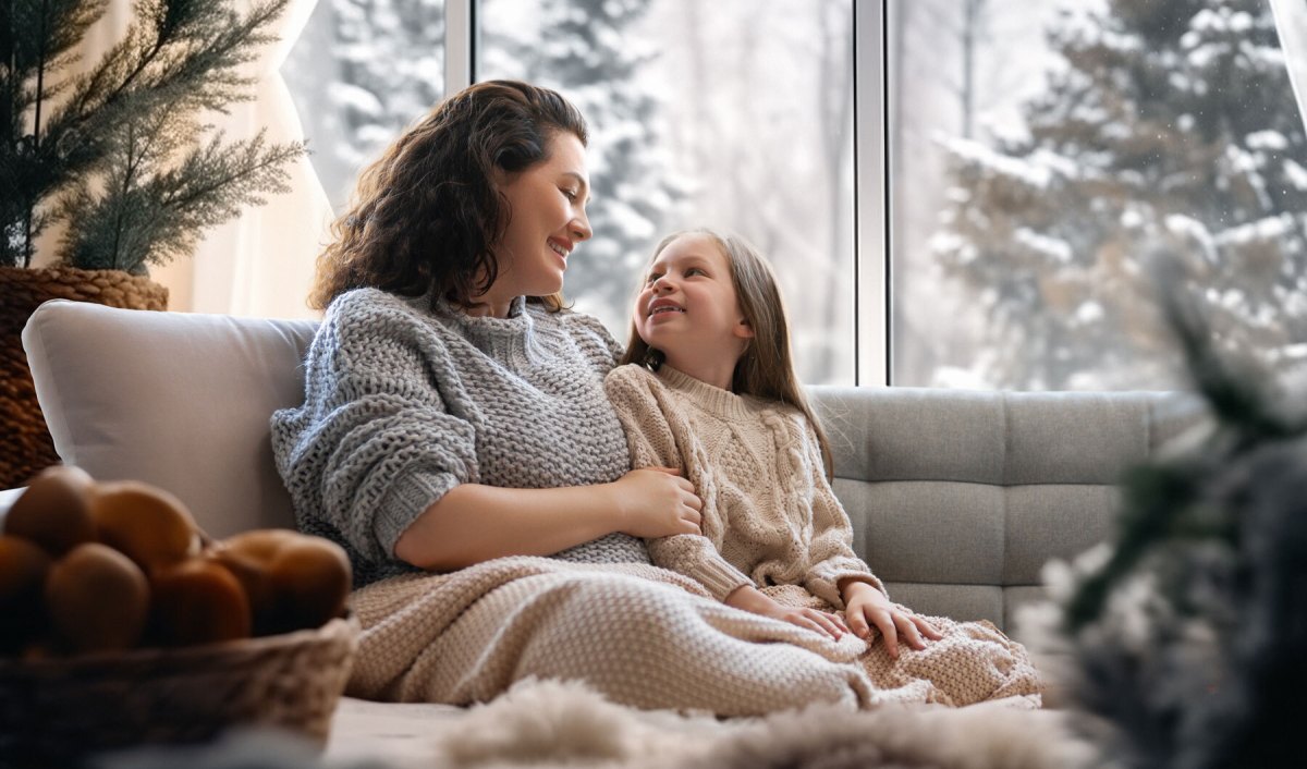 Mutter und Tochter sitzen eingekuschelt in eine Decke auf dem Sofa und unterhalten sich.