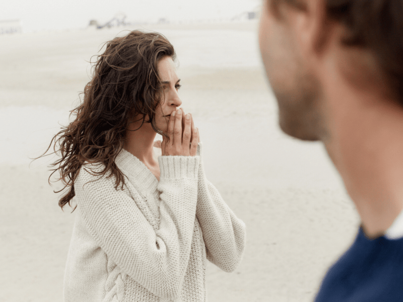 Frau steht am Strand und schaut nachdenklich in Ferne.
