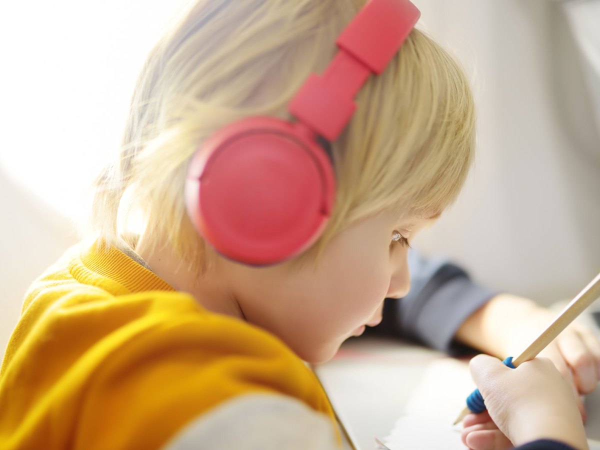 Kind, ca. 5 Jahre, sitzt im Flugzeug, hat Kopfh&ouml;rer auf und zeichnet gedankenversunken auf einem Blatt Papier.