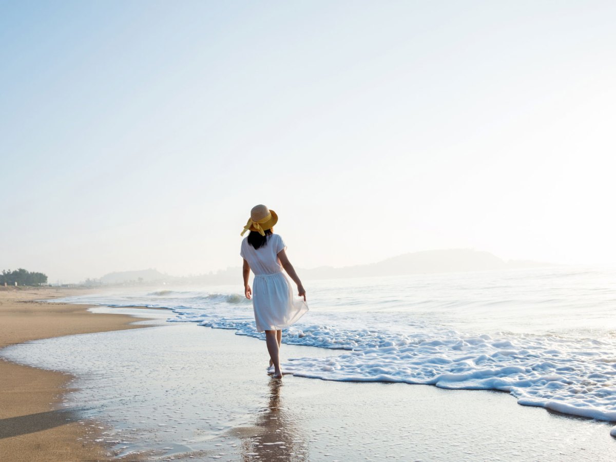 Frau im Sommerkleid mit Sonnenhut am Strand