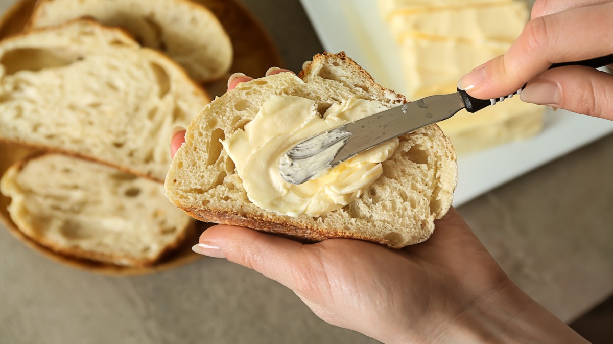 Person schmiert Butter oder Margarine auf eine Scheibe Brot.