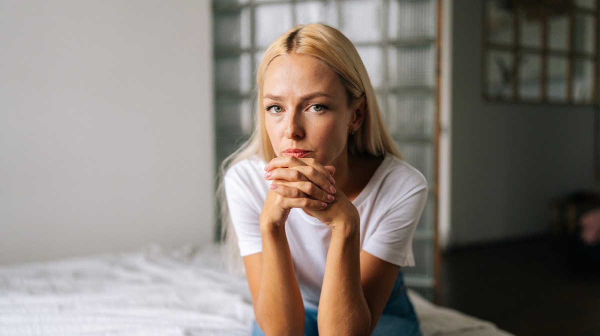 Blonde Frau auf einem Bett, die ernst und nachdenklich in die Kamera schaut