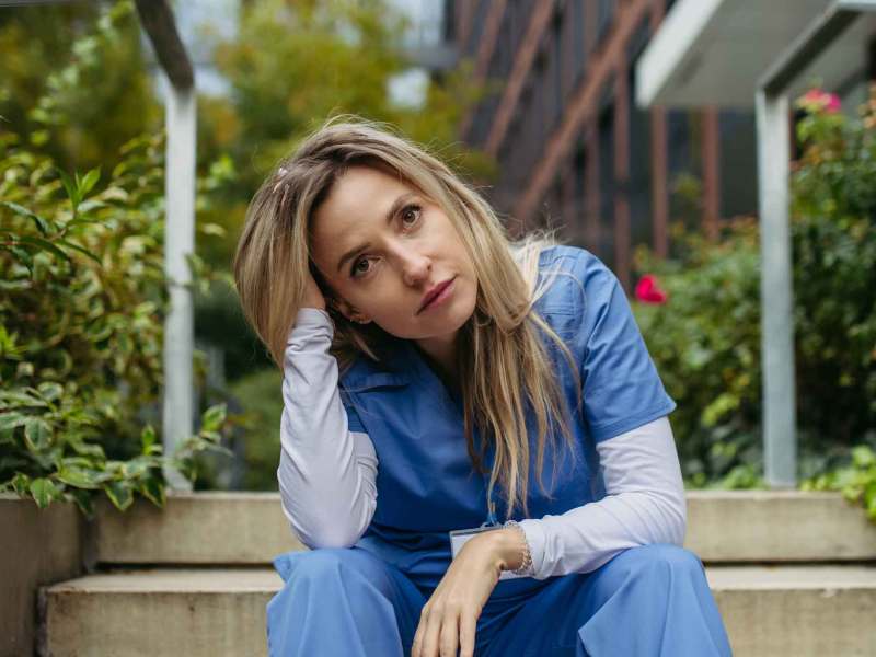 Junge Frau mit OP-Kasack sitzt drau&szlig;en und ist verzweifelt.