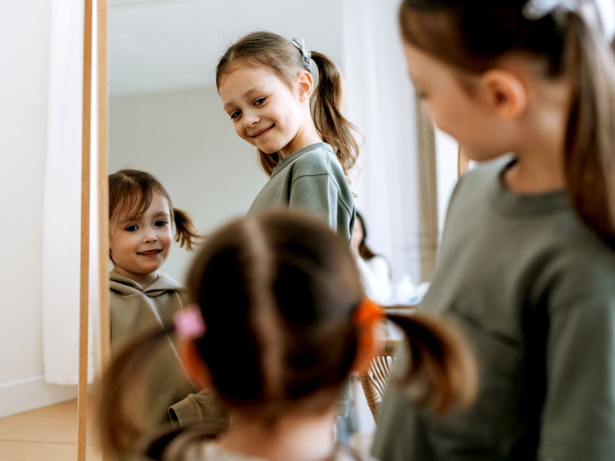 Zwei Schwestern stehen zu Hause vorm Spiegel und schauen sich an.
