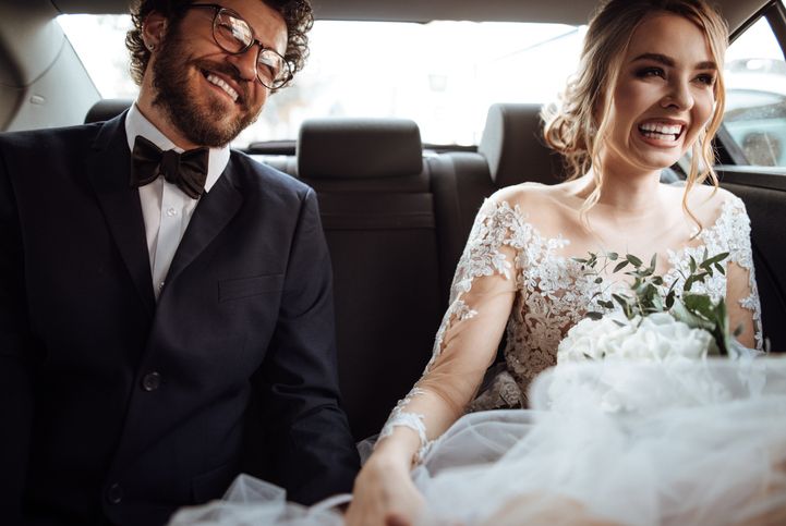 Brautpaar sitzt im Anzug und Brautkleid im Auto