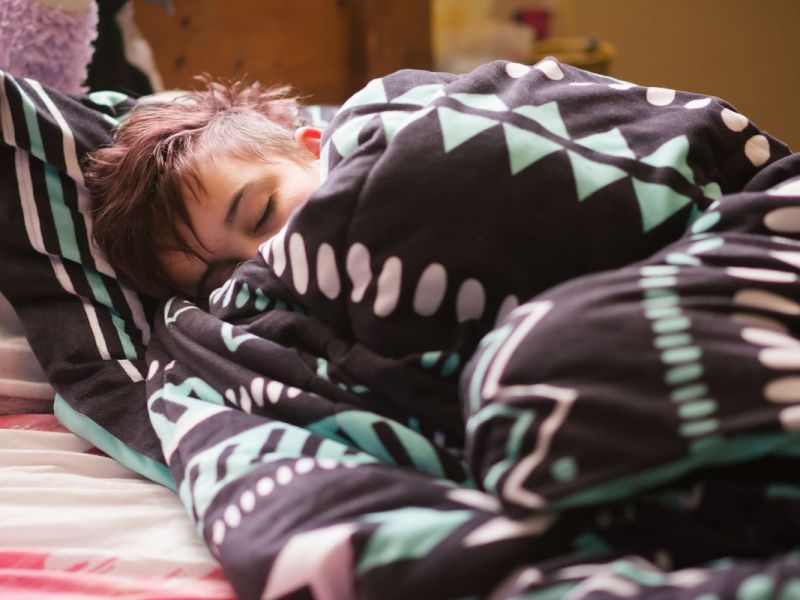 Teenager liegt tagsüber eingekuschelt in seinem Bett und schläft.