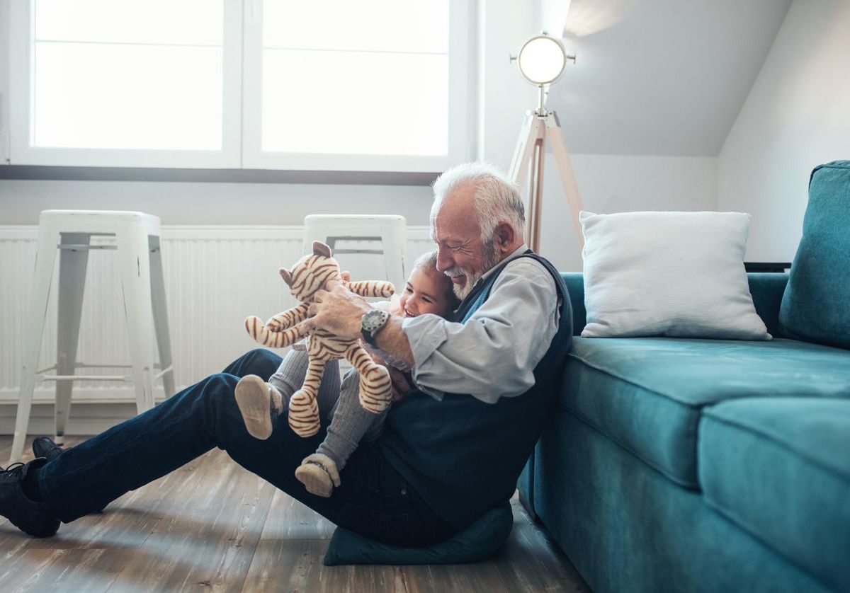 Großvater und Enkeltochter spielen im Wohnzimmer zusammen.