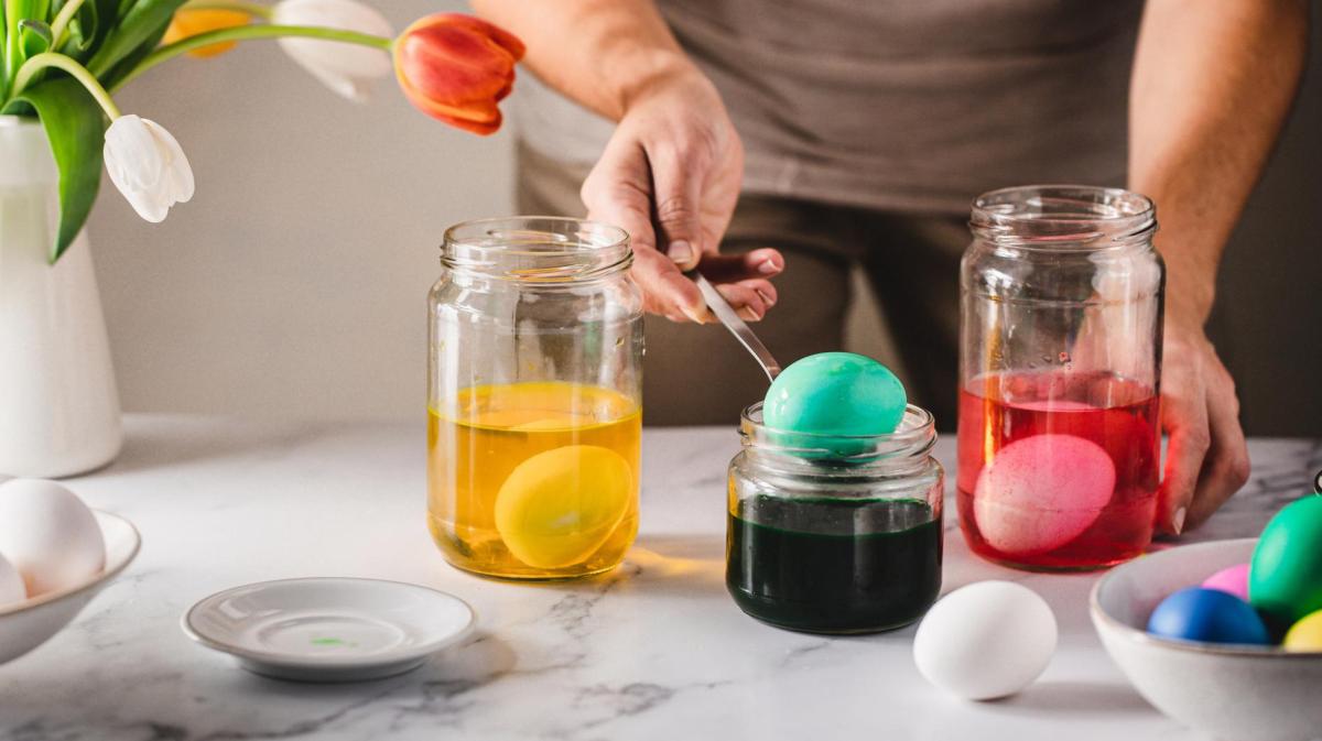 Frau färbt Eier in Gläsern.