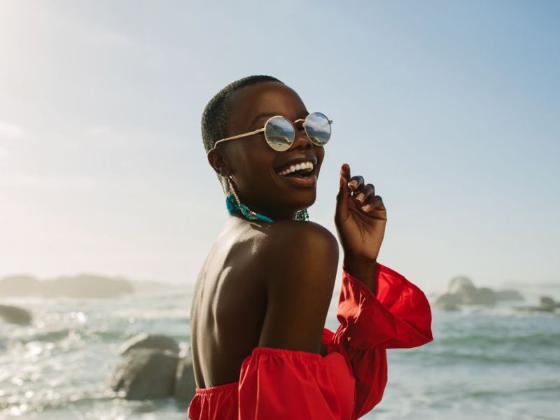 Frau am Strand mit Sonnenbrille am lachen