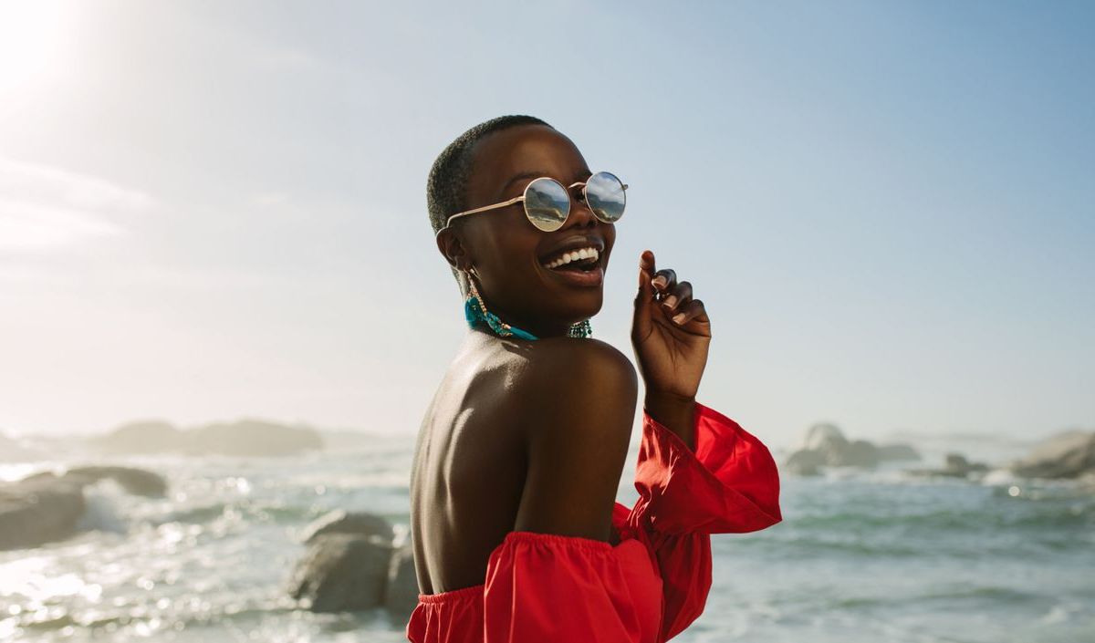 Frau am Strand mit Sonnenbrille am lachen