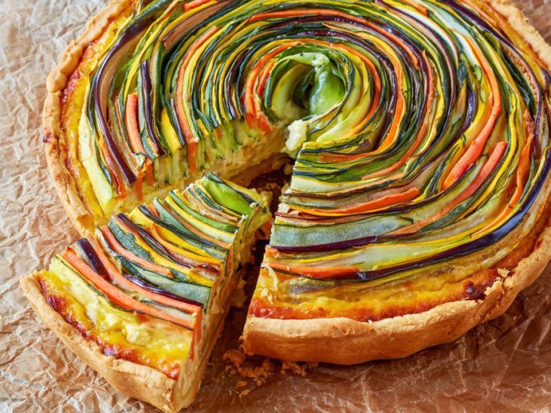 Bunte Spiral-Quiche mit verschiedenem Gemüse auf Backpapier.