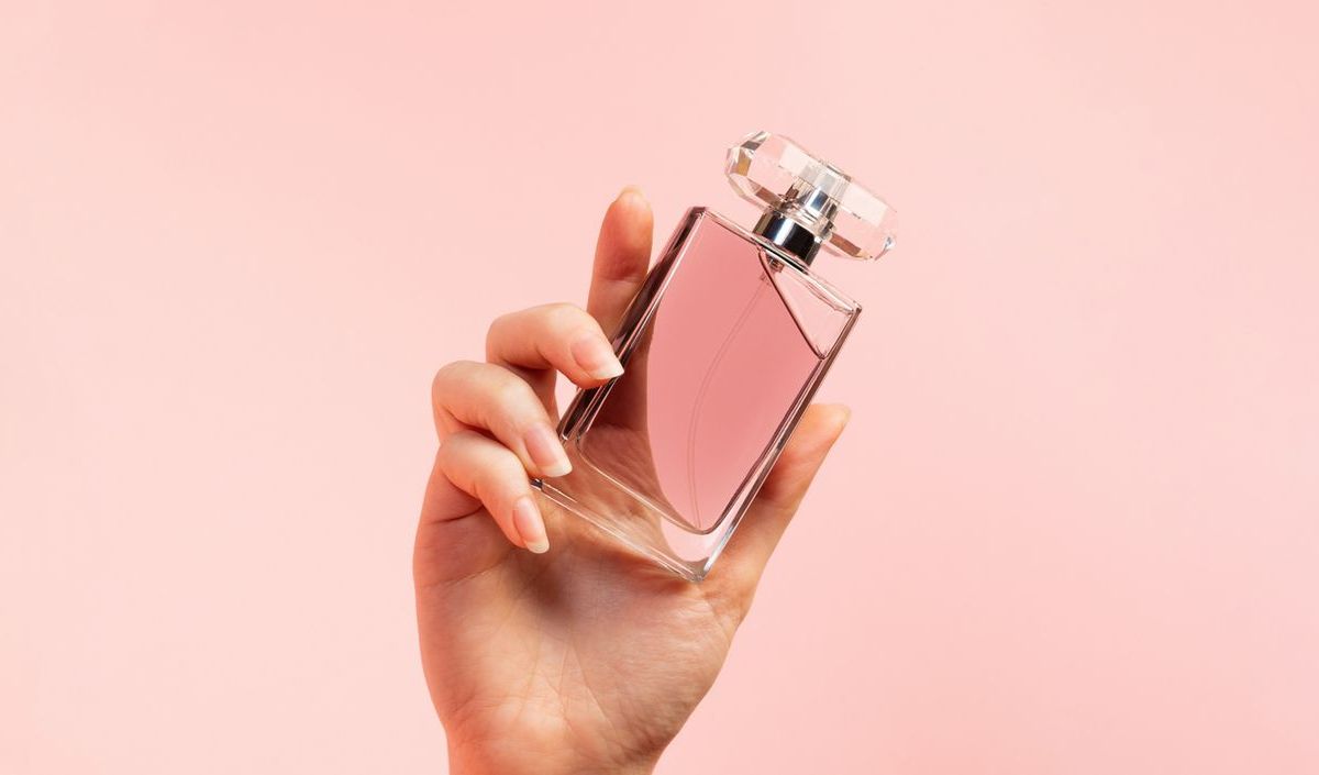 Frauenhand mit Parfum auf rosafarbenen Hintergrund