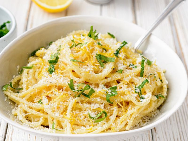 Weißer Teller mit Spaghetti, Zitronenabrieb und Parmesan.