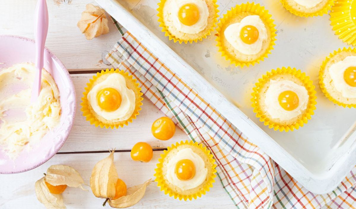 Cupcakes mit Creme und Physalis-Hälfte obendrauf auf Backblech.