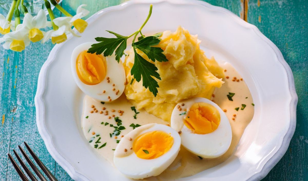 Hart gekochte Eier mit Senfsoße und Kartoffelpüree auf weißem Teller.