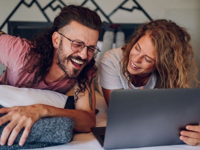 Pärchen auf dem Bett, lachend, mit Laptop