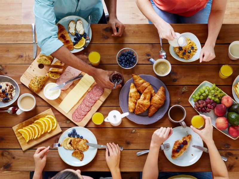 Eine Gruppe von Menschen sitzt gemeinsam am Tisch und frühstückt zusammen