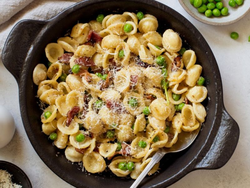 Nudeln mit Erbsen, Speck und Parmesan in einer schwarzen Gusseisenpfanne.