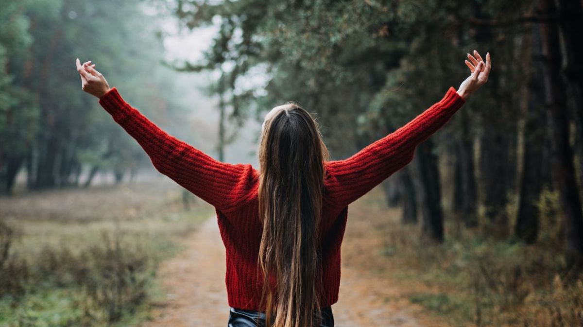 Frau mit langen braunen Haaren steht im Wald.