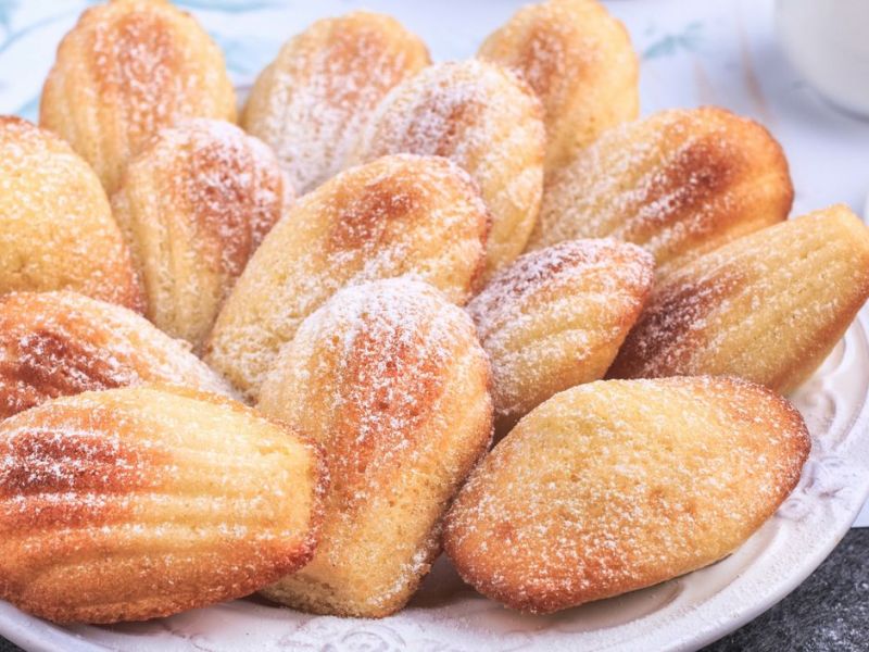 Selbst gemachte Madeleines mit Puderzucker auf einem weißen Teller.