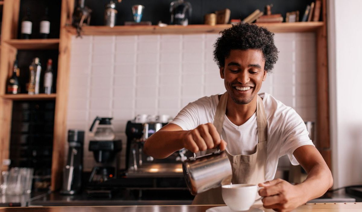 Barista bereitet lächelnd einen Cappuccino vor