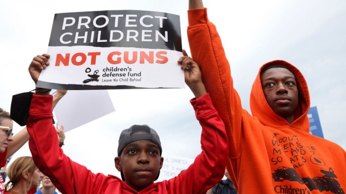 Ein kleiner Junge hält ein Protest-Schild hoch mit der Aufschrift "Schützt Kinder, nicht Waffen". 