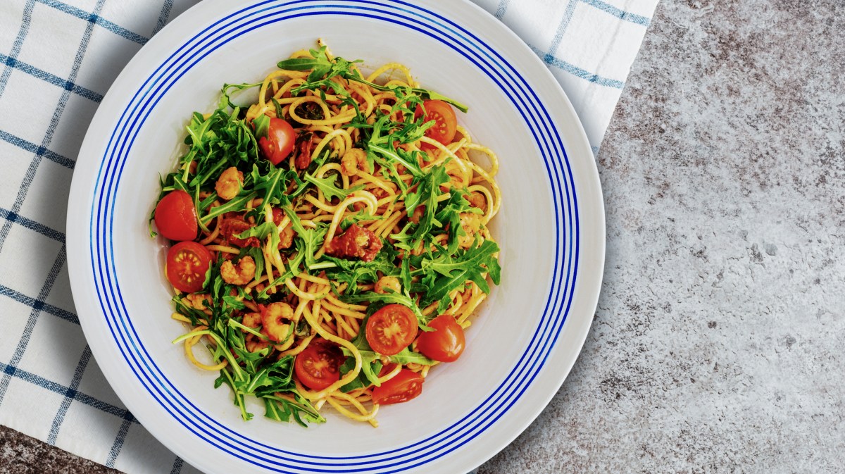 Spaghetti mit Rucola und Tomaten auf einem weißen Teller mit blauem Rand