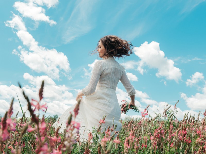 Frau im Kleid, die durch ein Blumenfeld geht