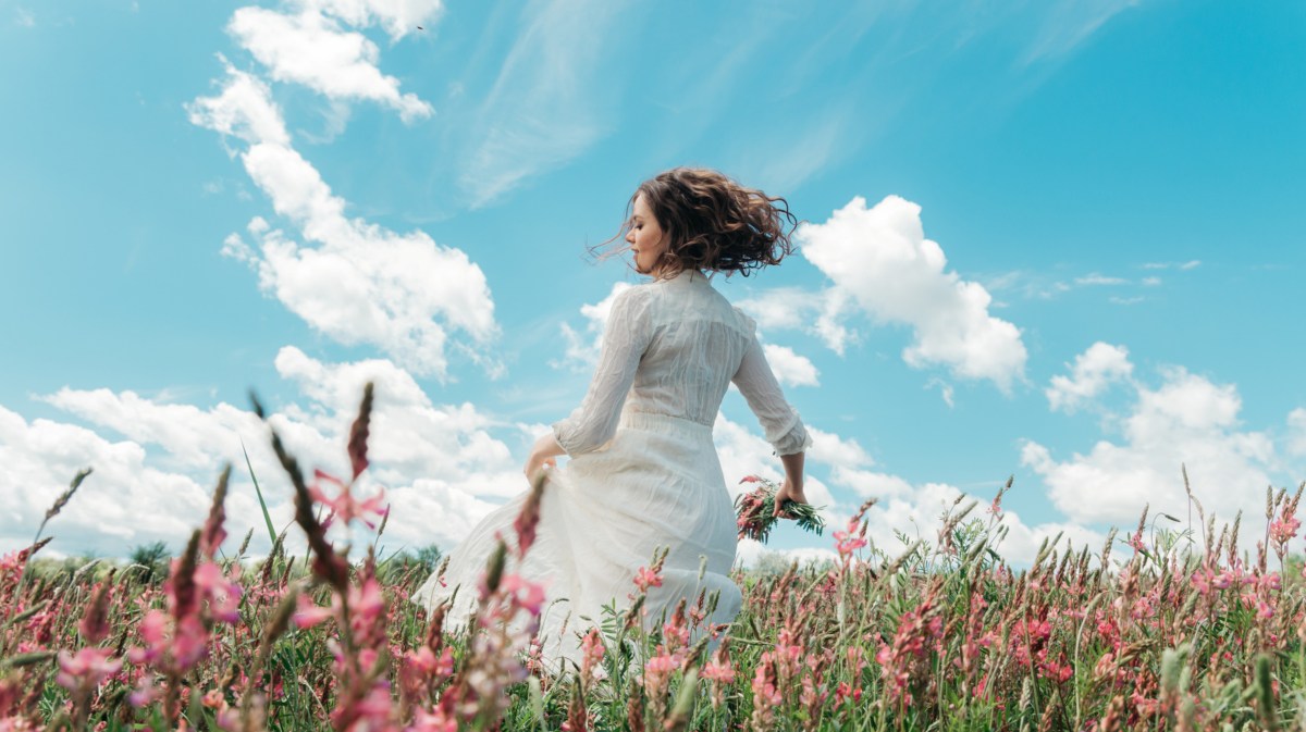 Frau im Kleid, die durch ein Blumenfeld geht