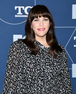 Der volle, gerade Pony von Liv Tyler verkürzt optisch die Stirn, während glänzende Wellen das Gesicht weich umrahmen.