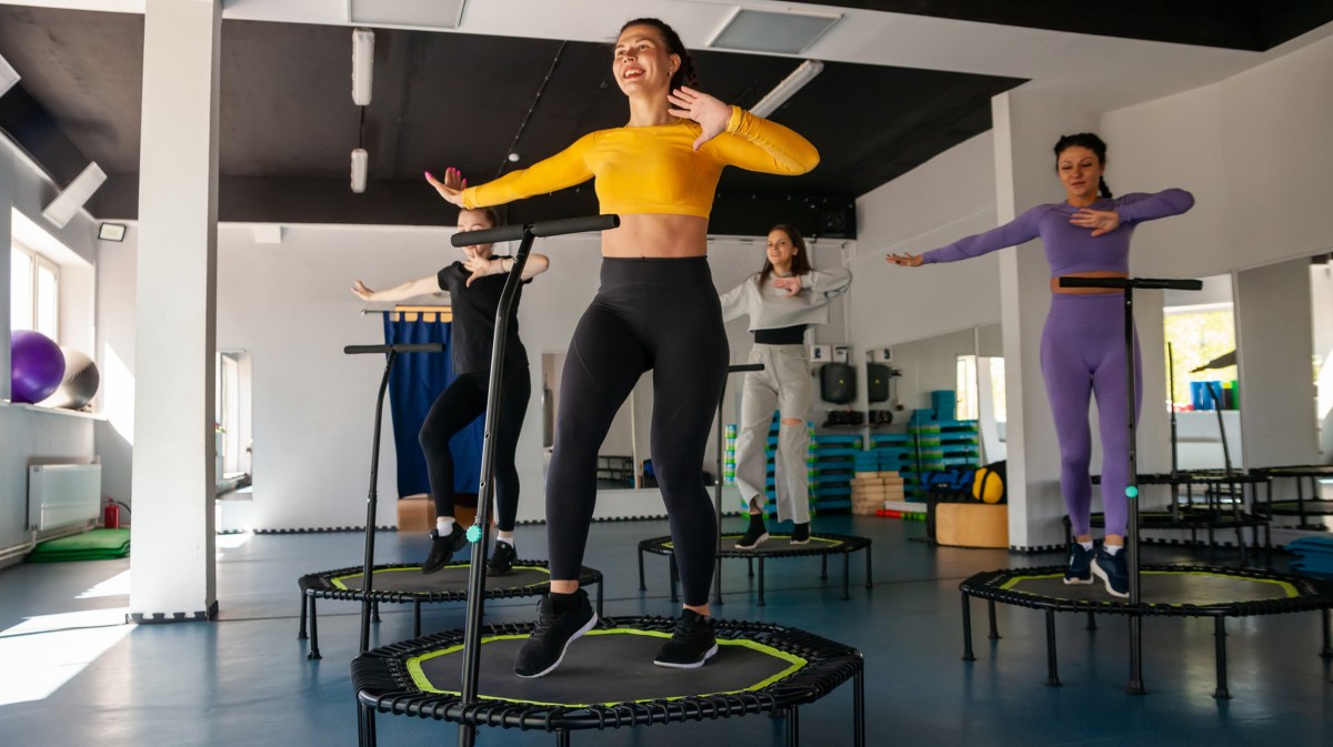 Vier Frauen, die in einem Fitnessstudio auf kleinen Trampolinen springen und dabei Tanzschritte ausführen.