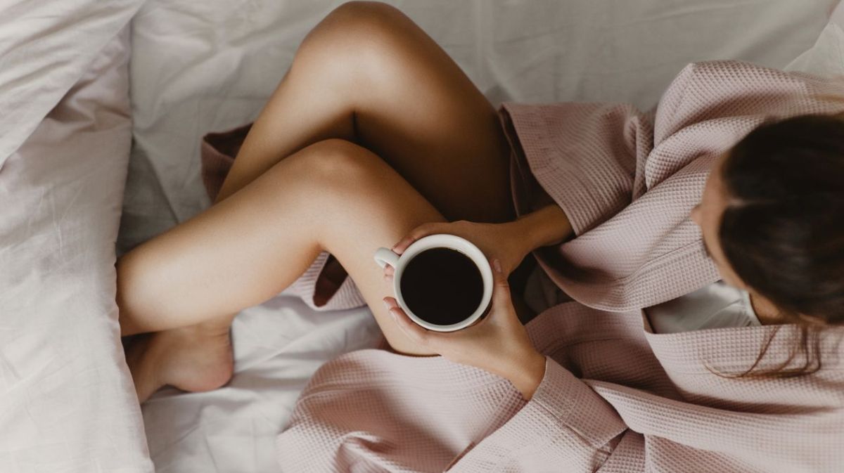 Frau liegt mit Tasse Kaffee im Bett