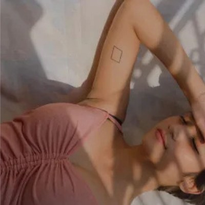 Frau in rosa Oberteil mit Rechteck Tattoo am Oberarm