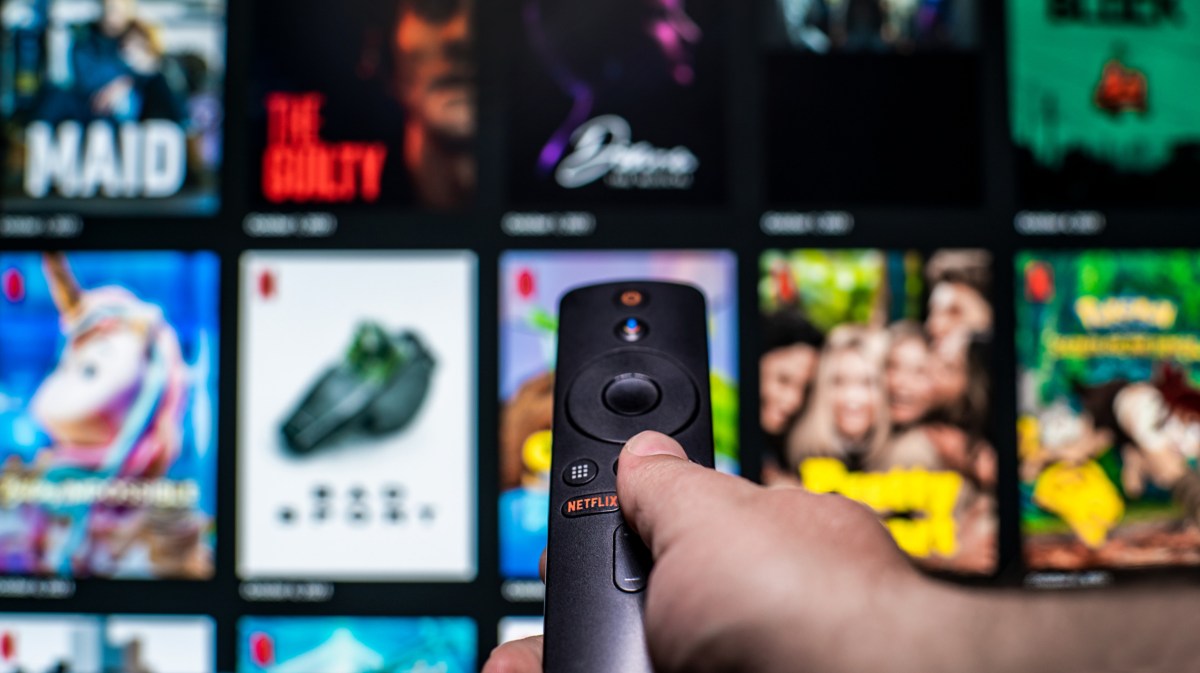 Mann mit Fernbedienung in der Hand und einem Netflix Bildschirm im Hintergrund