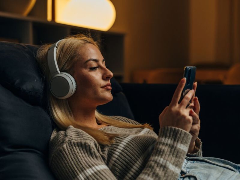 Frau sitzt gemütlich auf der Couch mit Handy in der Hand