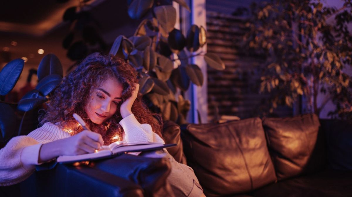 Frau sitzt in der Nacht auf dem Sofa und schreibt in ein Buch 