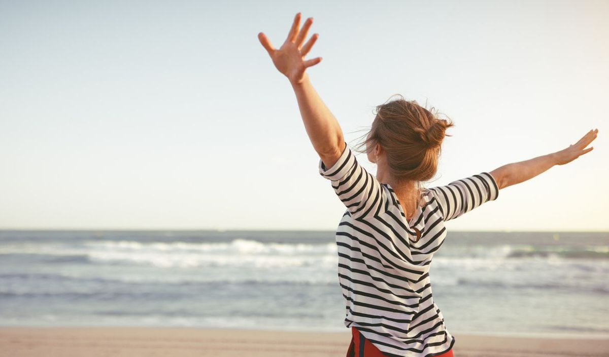 Frau mit ausgebreiteten Armen am Strand 