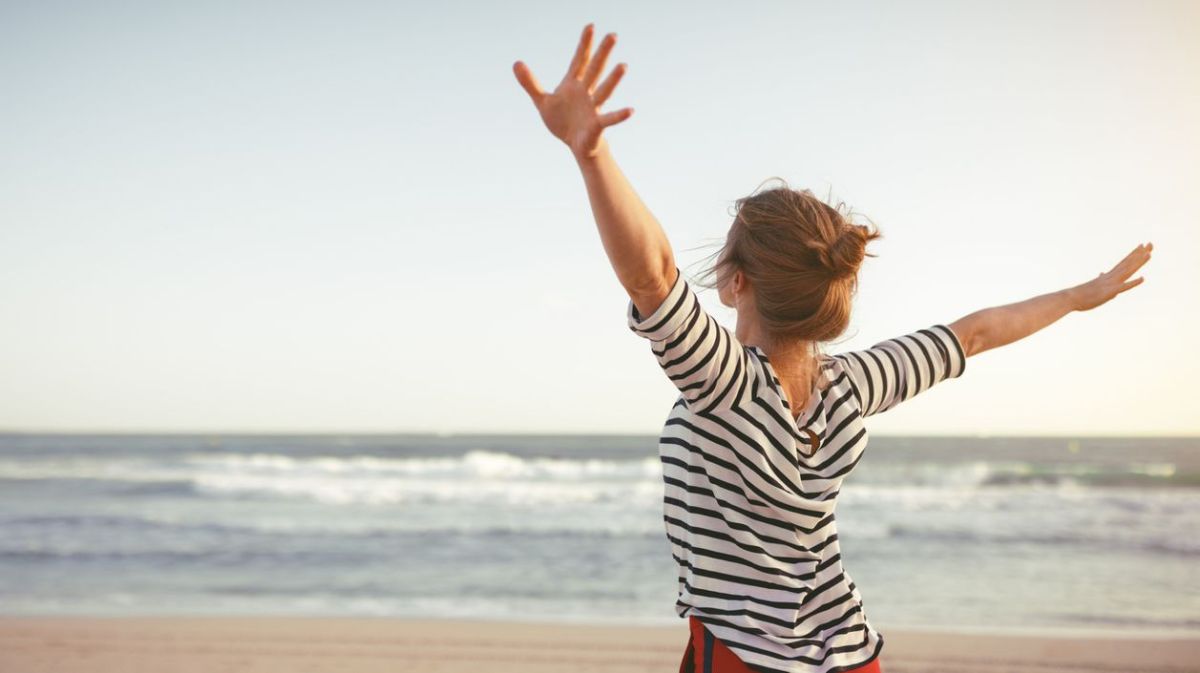 Frau mit ausgebreiteten Armen am Strand 