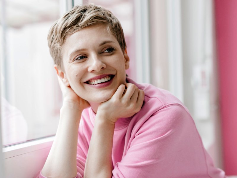 Kurzhaarfrisuren: Frau mit kurzem Haarschnitt und rosa Pullover lächelt