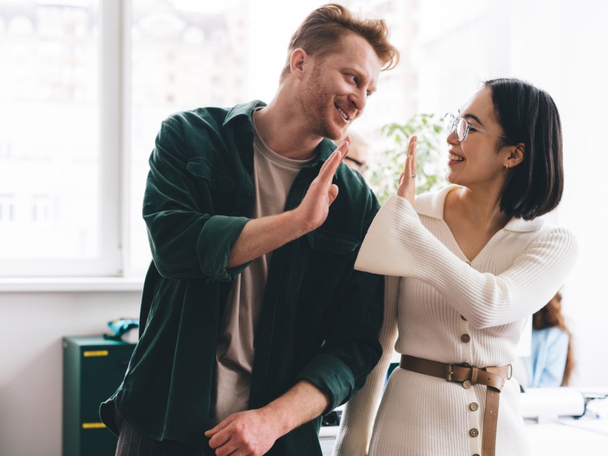 Junger Mann und Frau geben sich auf Arbeit ein High Five.