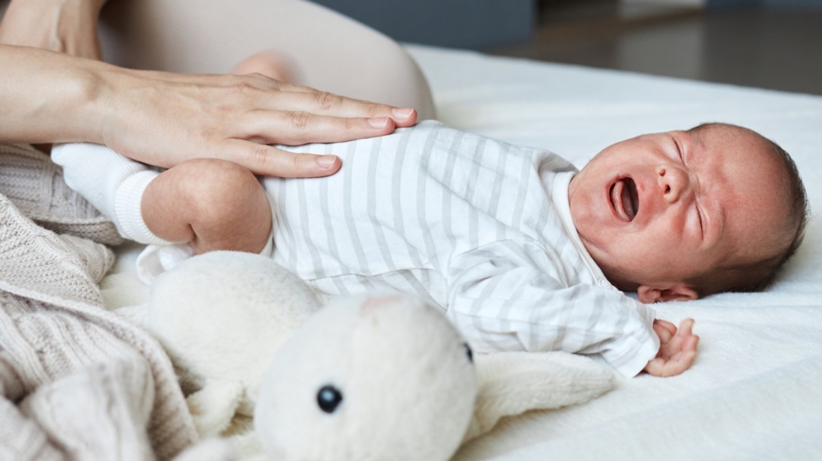 Ein weinendes Baby auf dem Bett wird von der Mutter gestreichelt.