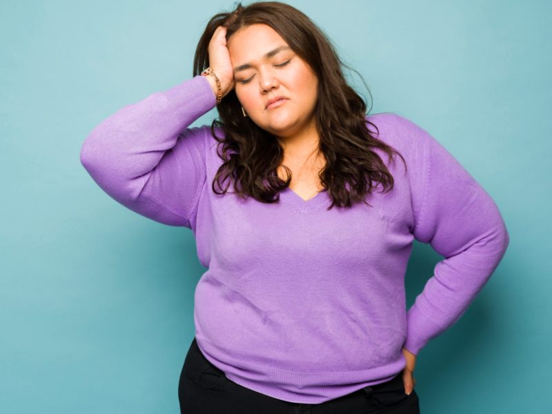 Frau mit lila Oberteil h&auml;lt sich den Kopf wegen Stress; muss Cortisol senken