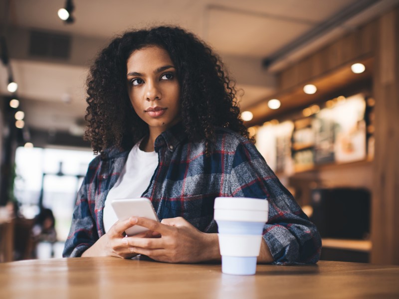 Frau sitzt nachdenklich in einem Café mit Handy in der Hand